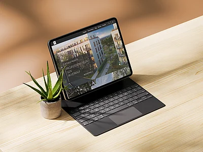 Tablet mit Tastatur auf hellem Tisch, daneben eine kleine Pflanze, auf dem Bildschirm eine Immobilien-Projektwebsite