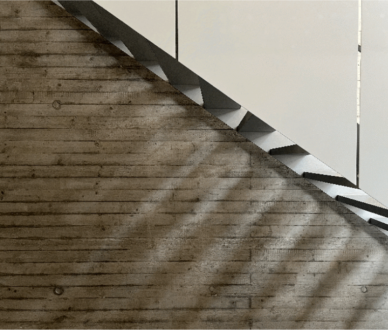 Seitenansicht einer Metalltreppe im Treppenhaus der Netzbewegung, die Schatten auf eine Sichtbetonwand wirft.