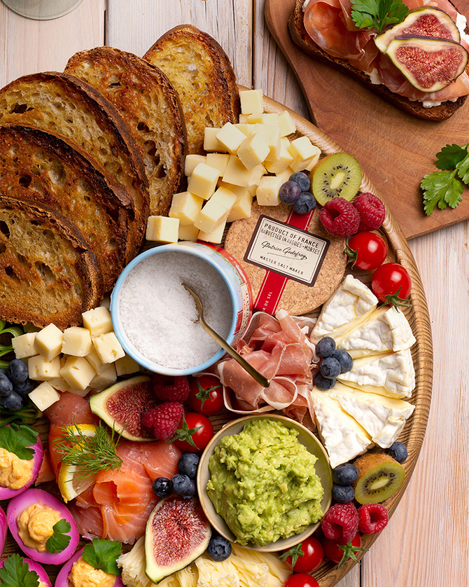 Große Platte mit Käse, Brot, Obst, Aufstrichen, Aufschnitt und mit grobem Meersalz in einer Salzpackung von Le Saunier de Camargue von oben fotografiert