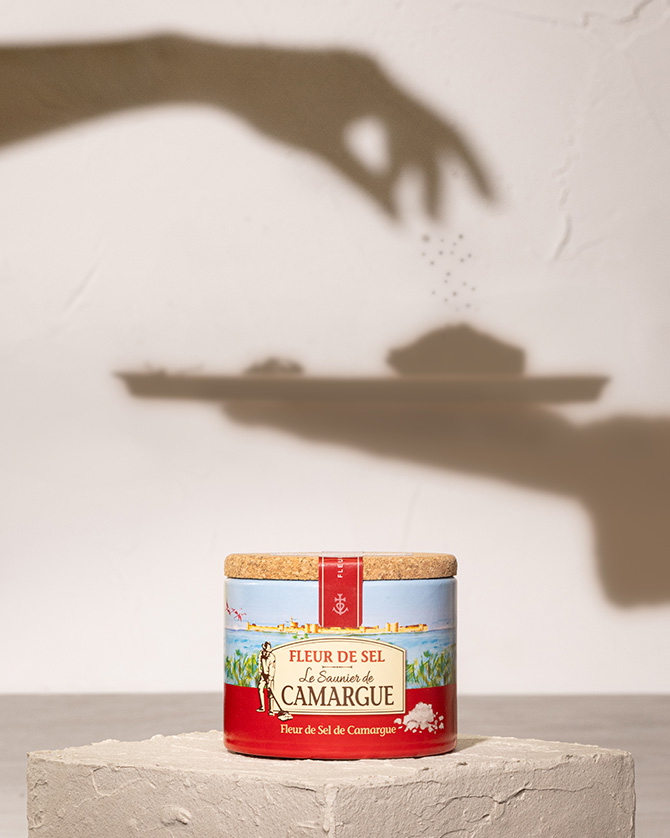 Dose Meersalz von Le Saunier de Camargue auf Podest, darüber der Schatten einer Hand beim Salzen