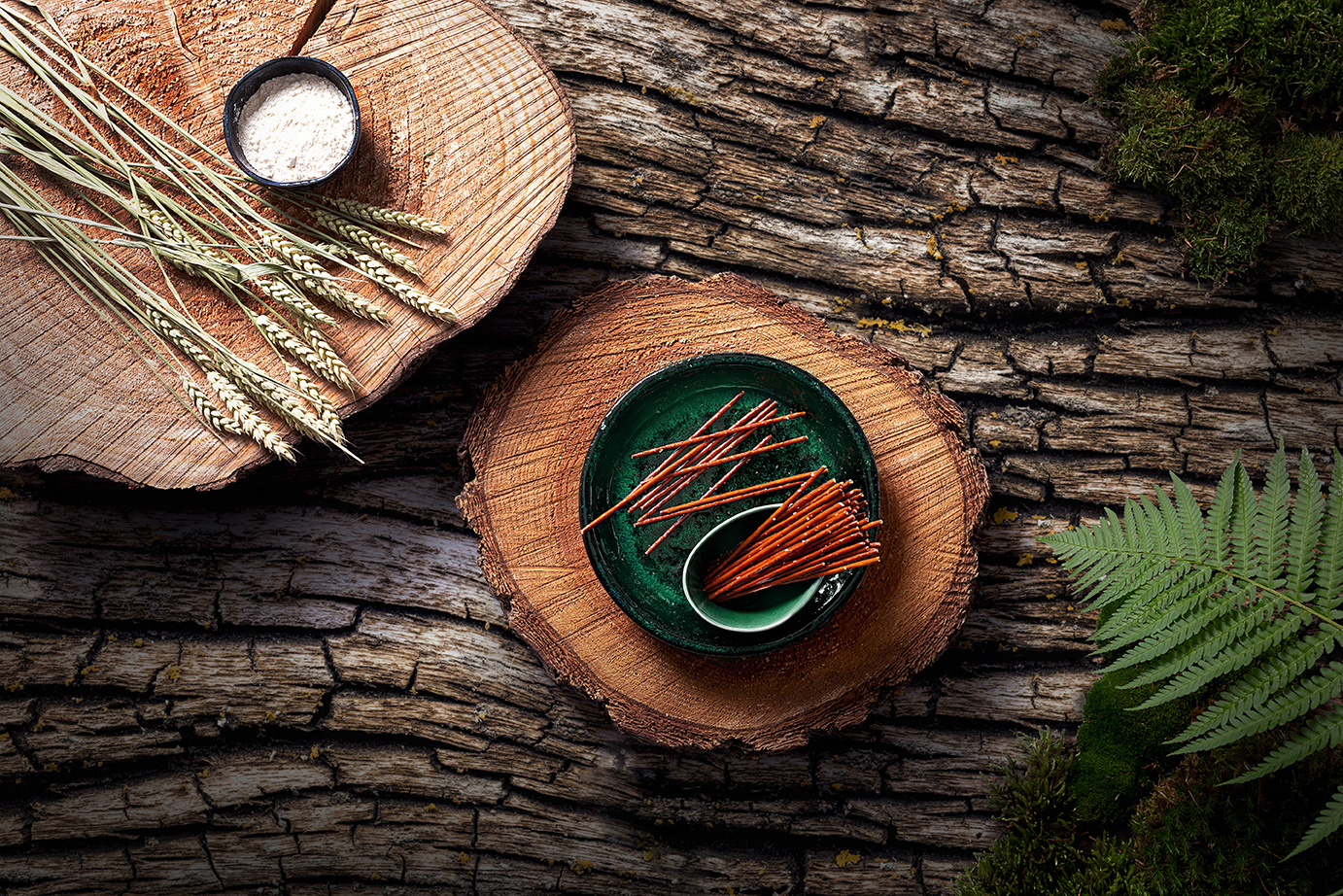 Foto von der Draufsicht auf eine Schale MAYKA Sticks auf einer Holzscheibe. Daneben sind Strohalme und eine Schale mit Salz drapiert. Der Untergrund ist eine grobe Rindenstruktur.