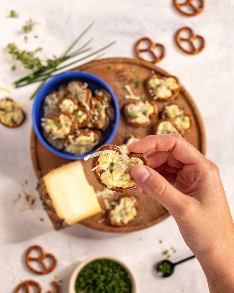 Eine Hand greift sich eine mit Käse überbackende Brezeln von einem Brotzeitbrett.