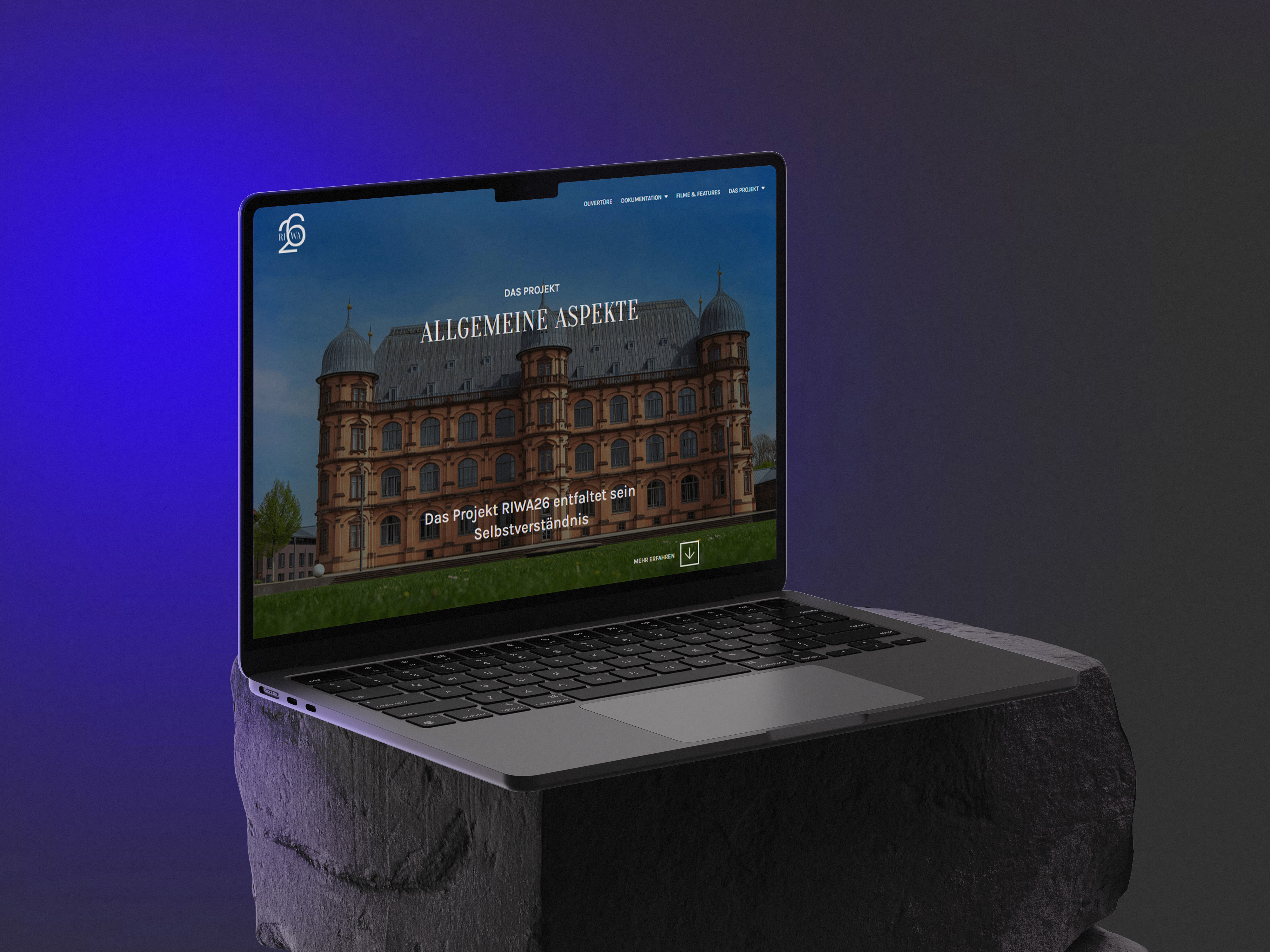 Ein moderner Laptop steht leicht angewinkelt auf einem steinartigen Podest vor einem dunklen Hintergrund mit violettem Licht. Auf dem Bildschirm ist eine Website mit dem Gebäude der HfM Karlsruhe zu sehen und der Titel „Allgemeine Aspekte“ sowie weitere deutsche Navigationselemente enthält.