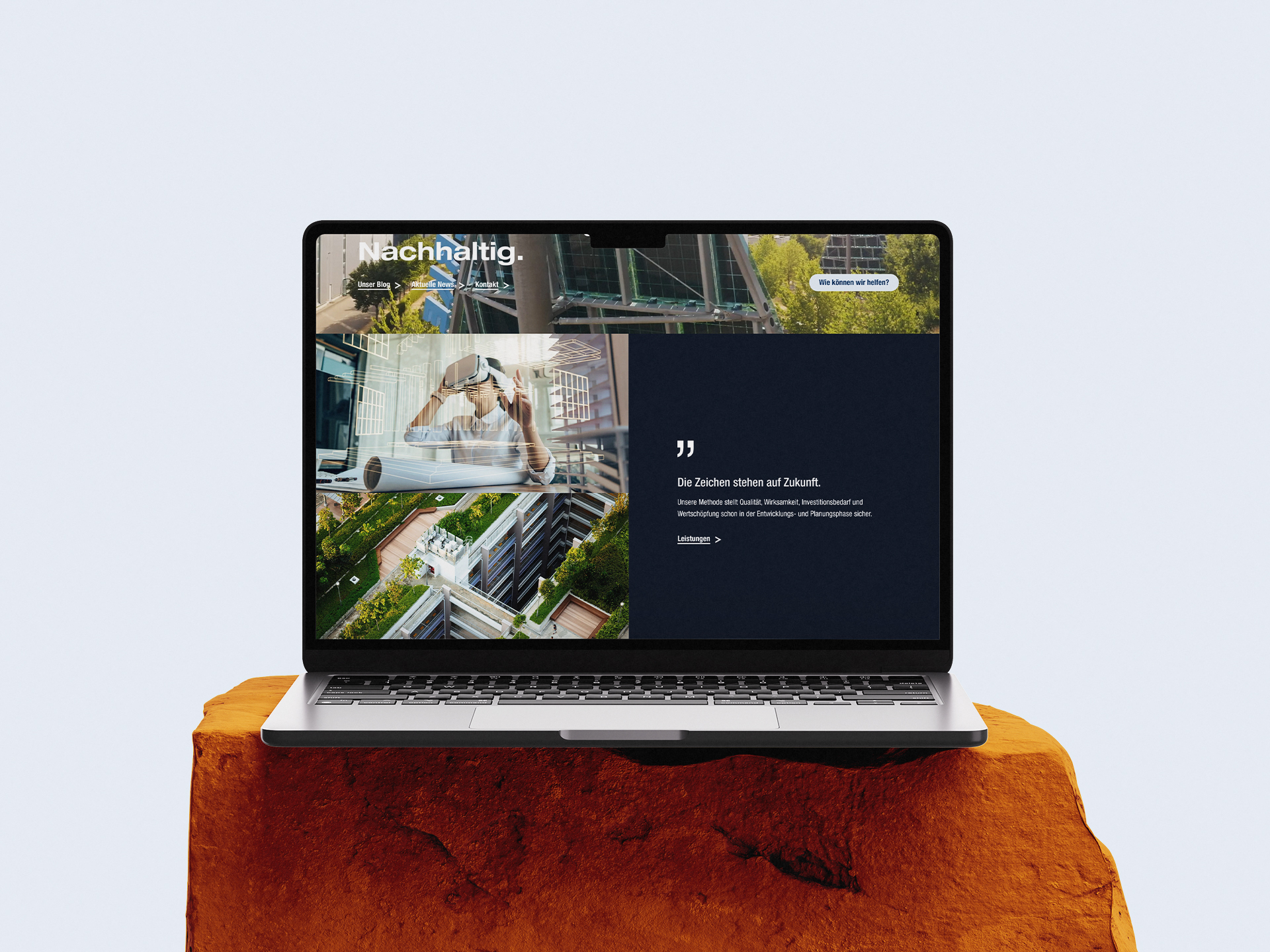 Laptop auf einem Felsblock vor hellem Hintergrund, auf dem Bildschirm die moderne Website von Vollack mit nachhaltiger Architektur, Stadtgrün und einem Menschen mit VR-Brille, ergänzt durch den Slogan „Die Zeichen stehen auf Zukunft.“