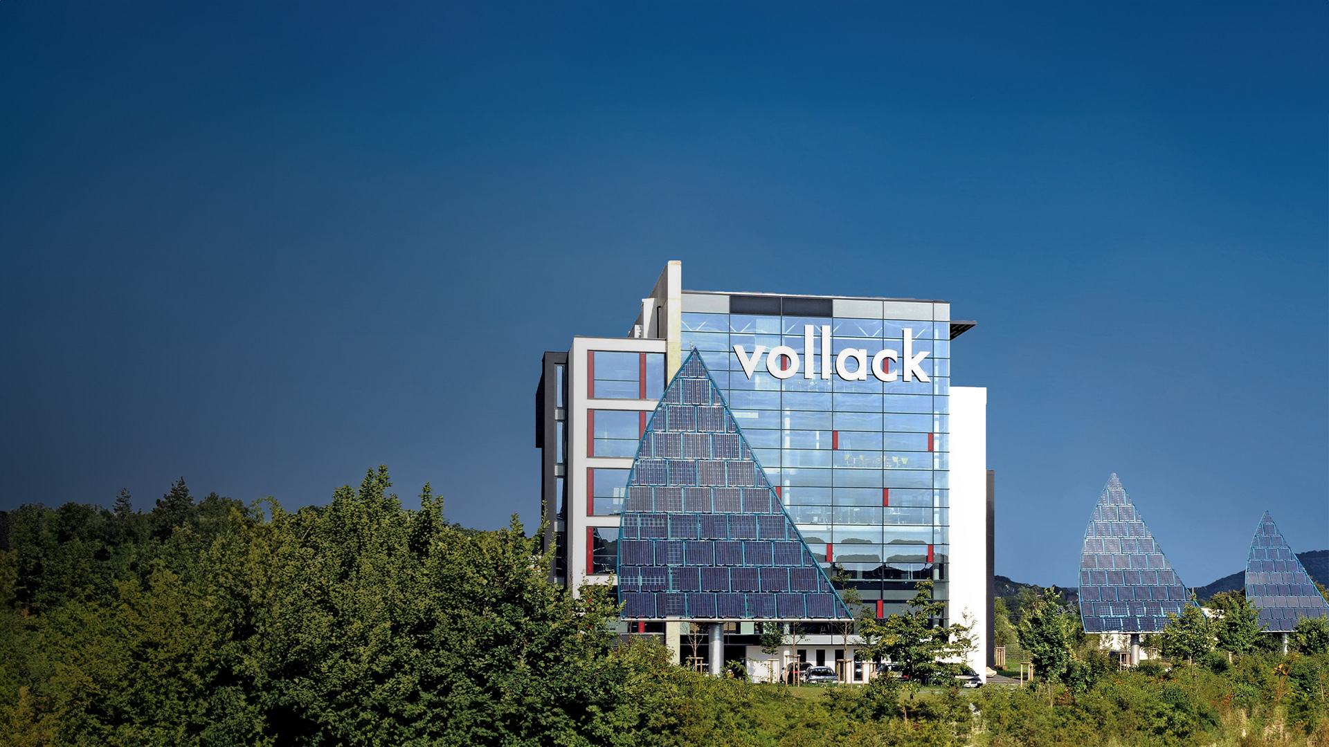 Panorama-Ansicht des Vollack-Firmengebäudes mit einem Photovoltaik-Segel vor blauem Himmel.