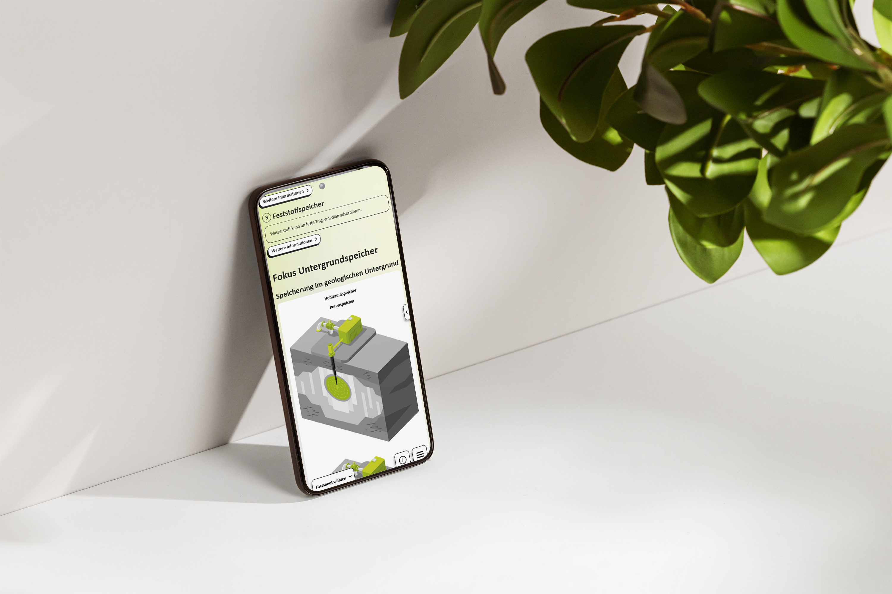 Smartphone auf einem weißen Schreibtisch mit Pflanzen, auf dem Bildschirm eine grafische Darstellung eines Kavernenspeichers zur Speicherung von Wasserstoff..